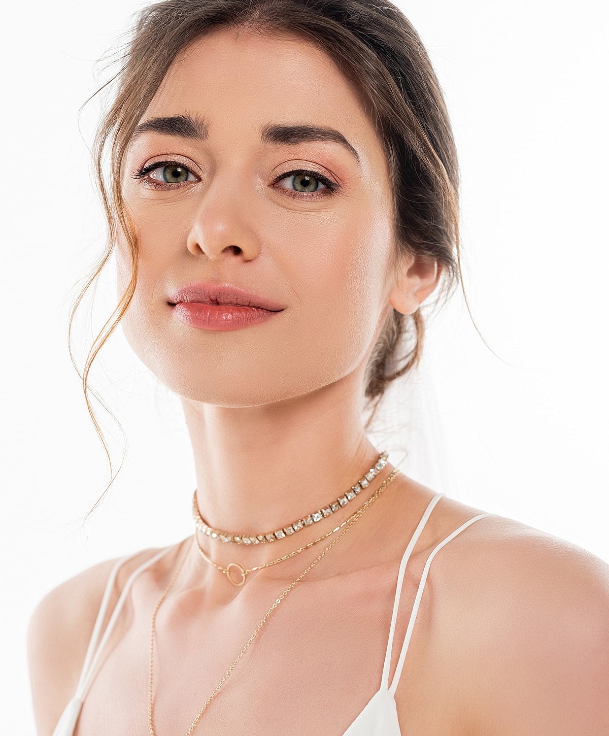 Woman in layered necklaces with a soft expression.