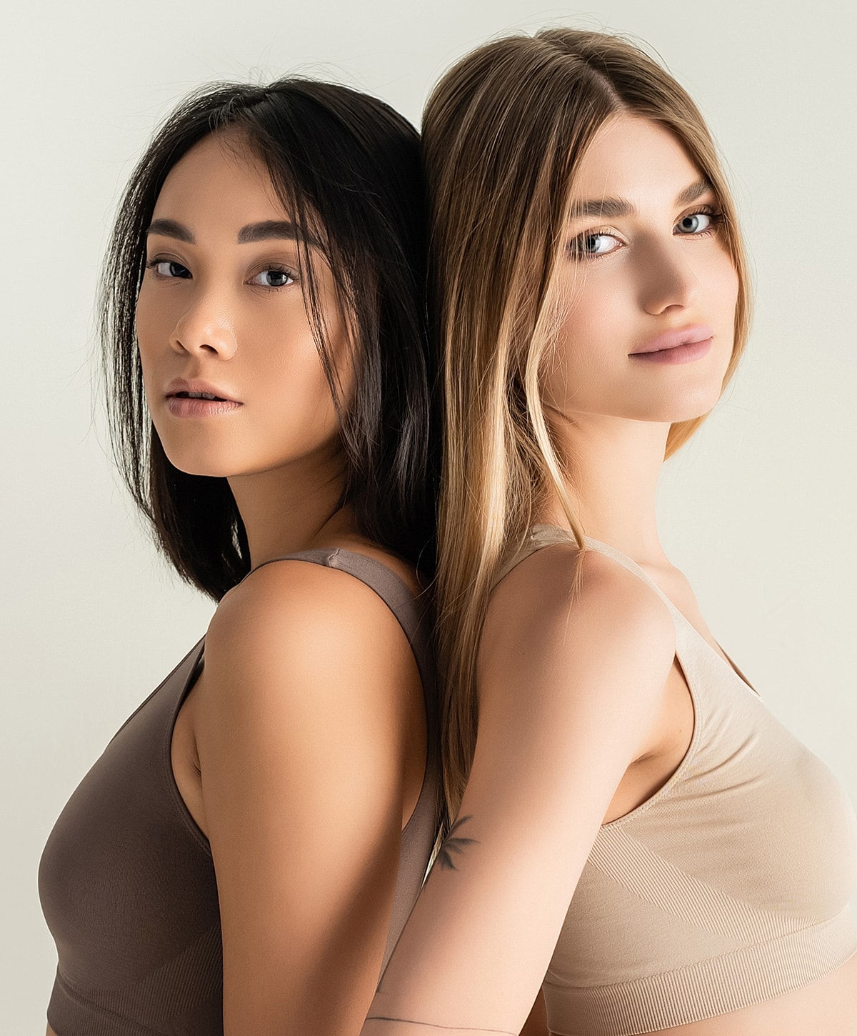 Two women posing back to back in bras.