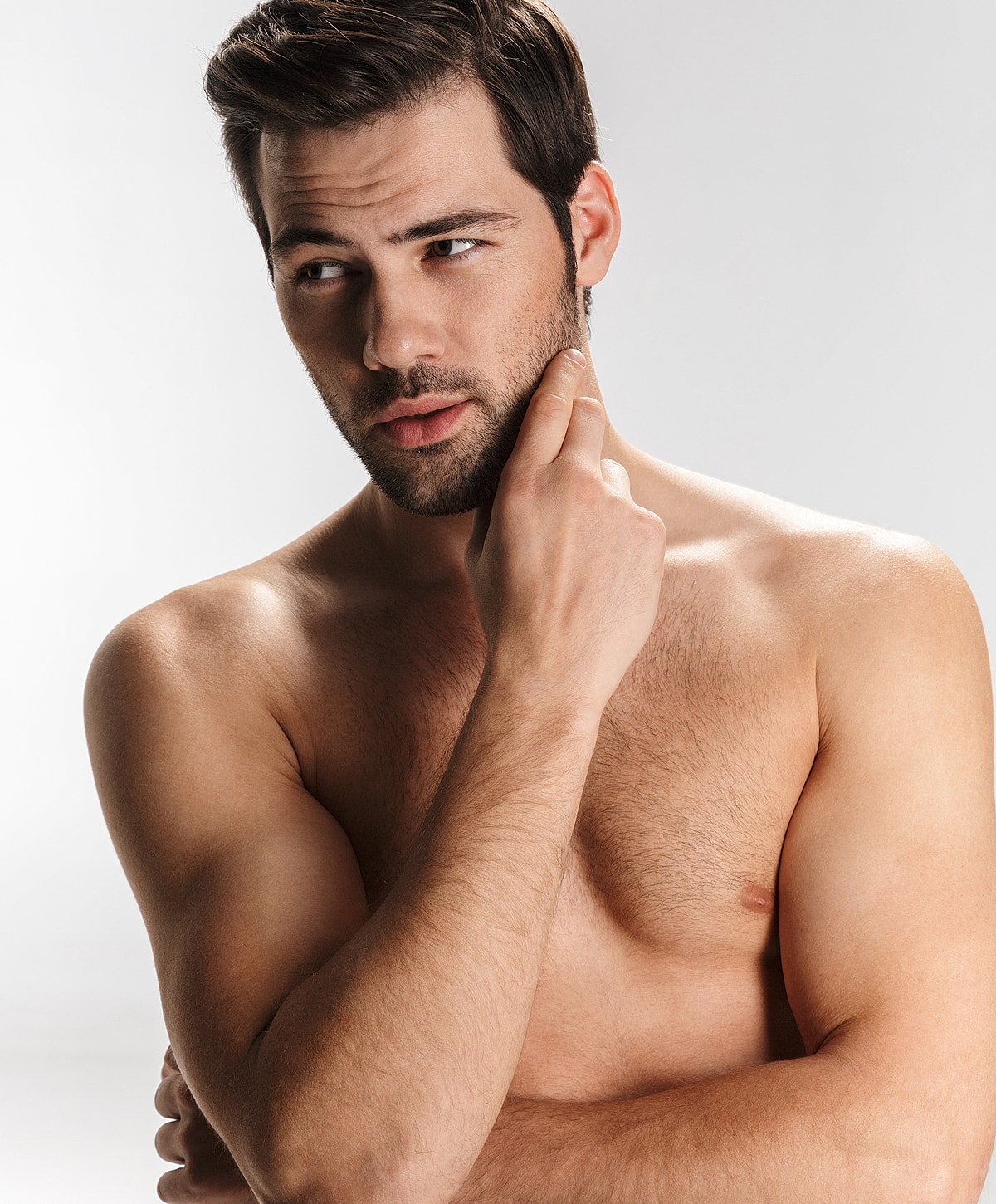 Man posing thoughtfully, shirtless against gray background.