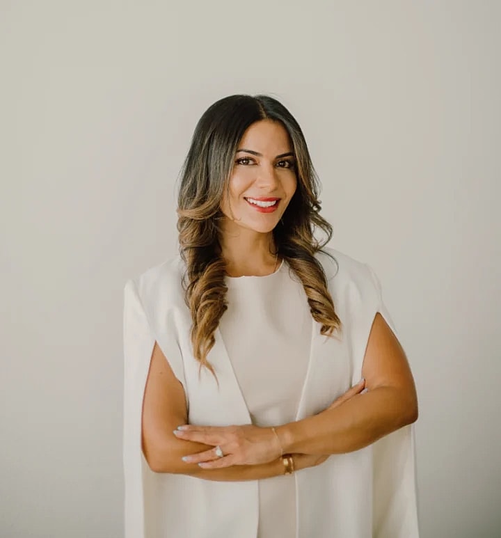 Smiling woman in white outfit, arms crossed.