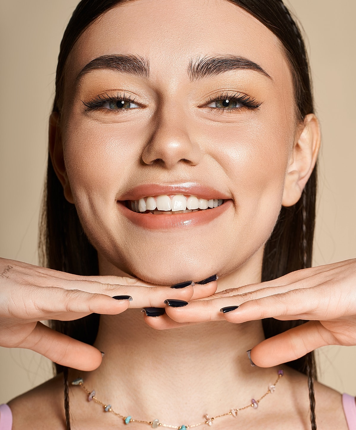 Smiling woman with hands under chin, neutral background.