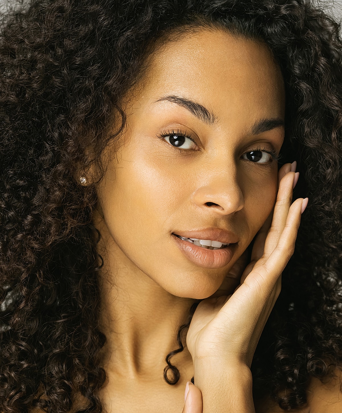 Woman with curly hair touching her face.