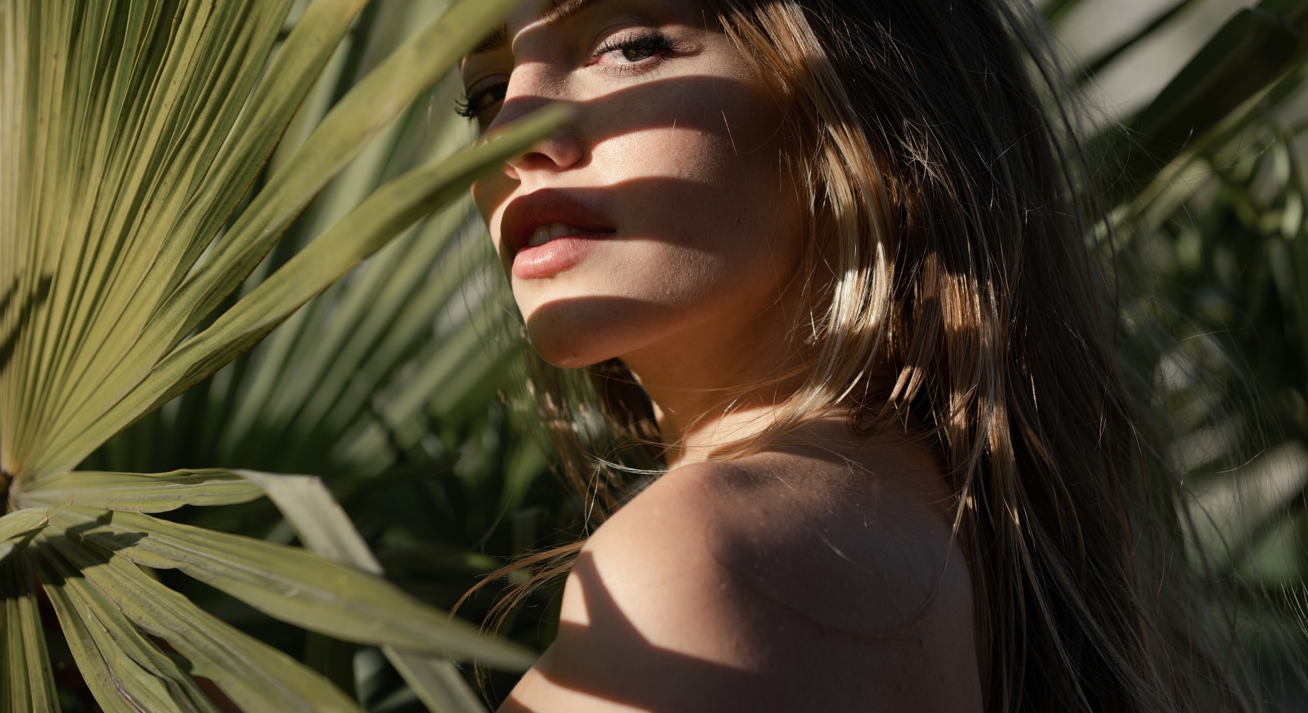 Woman in sunlight, surrounded by palm leaves.