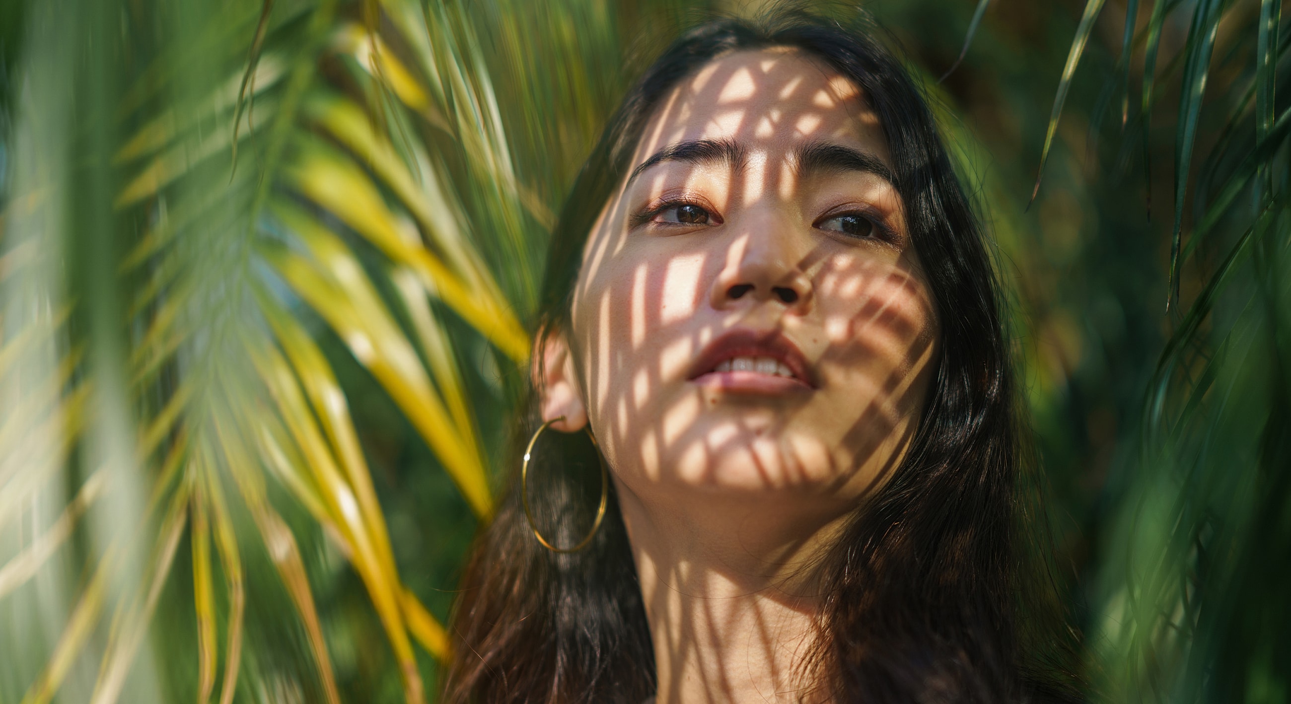 Woman's face with shadows from palm leaves.