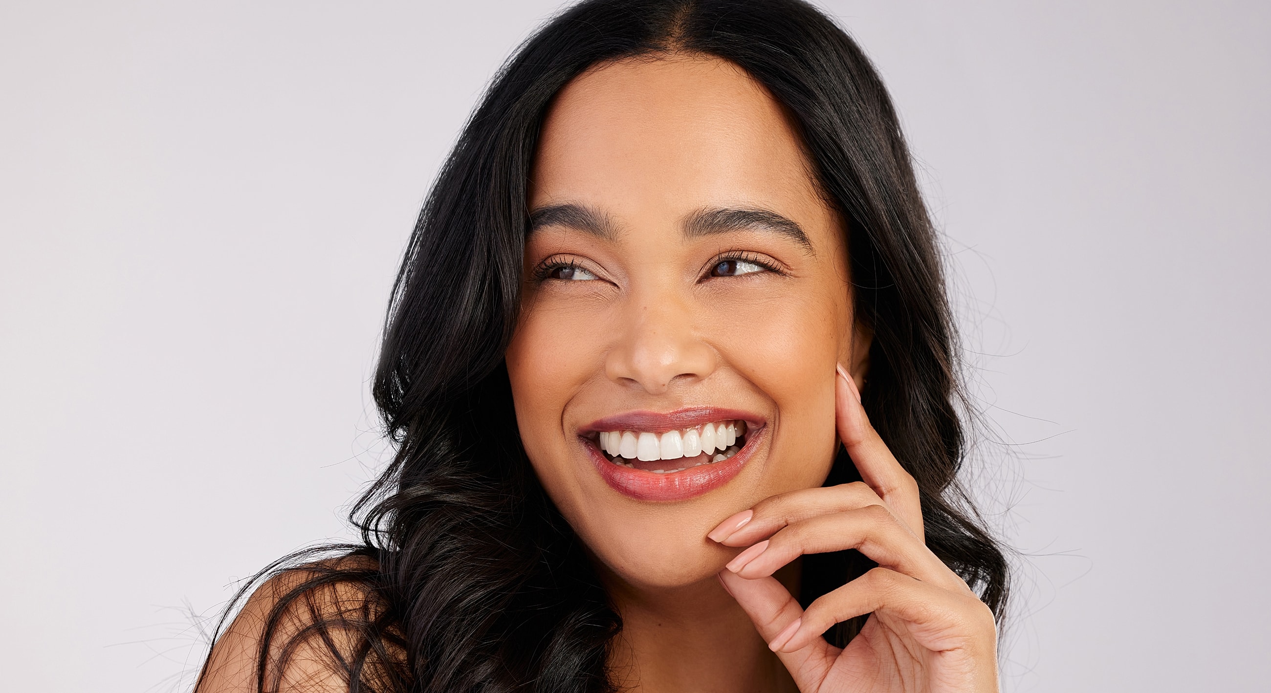 Smiling woman with long black hair, hand on face.